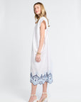 Woman wearing a white dress with blue lace details and white heels on a white background