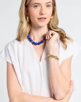 Woman wearing a white v-neck caftan with a blue beaded necklace on a white background
