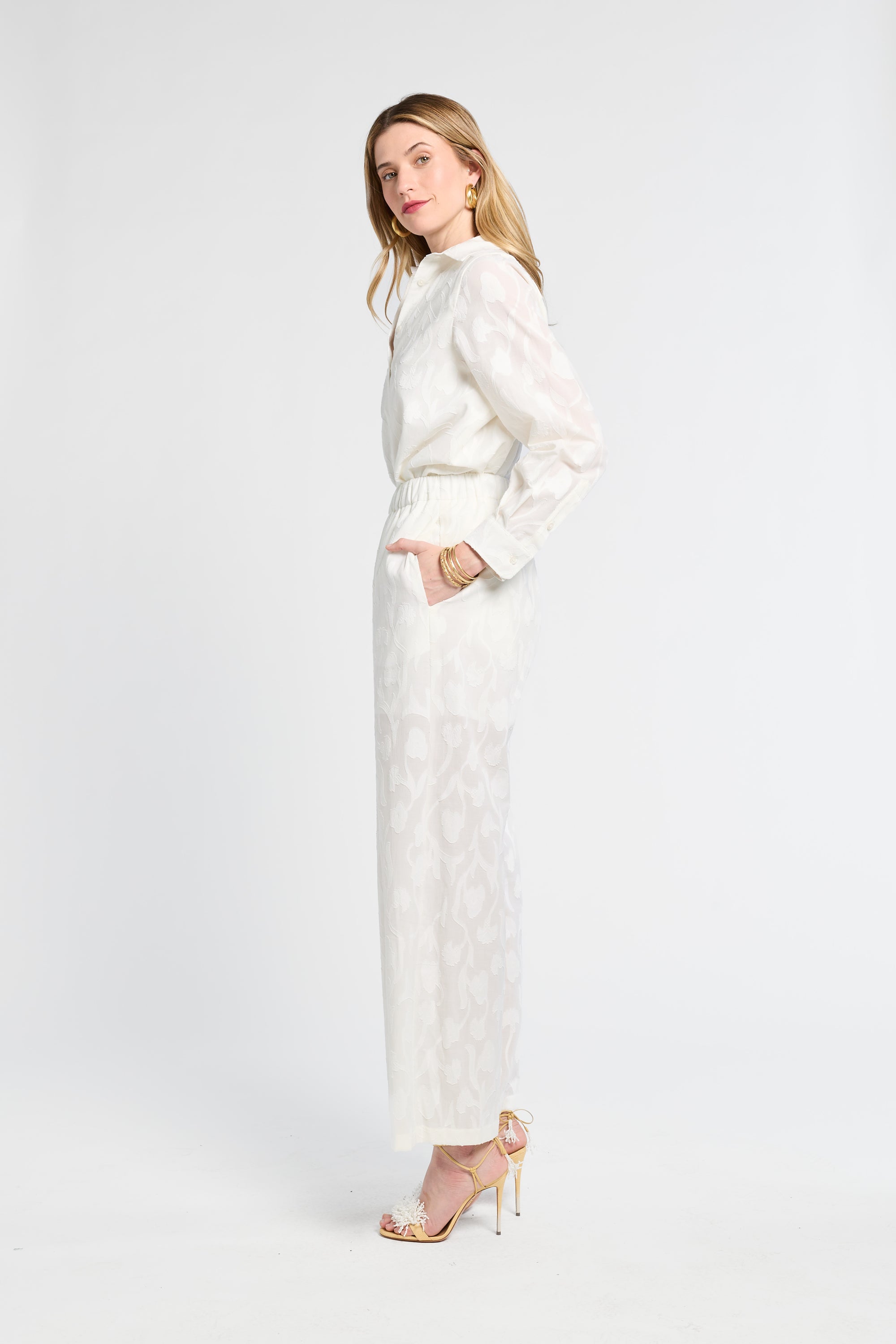 Woman modeling white floral pants wearing heels against a white background