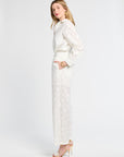 Woman modeling white floral pants wearing heels against a white background