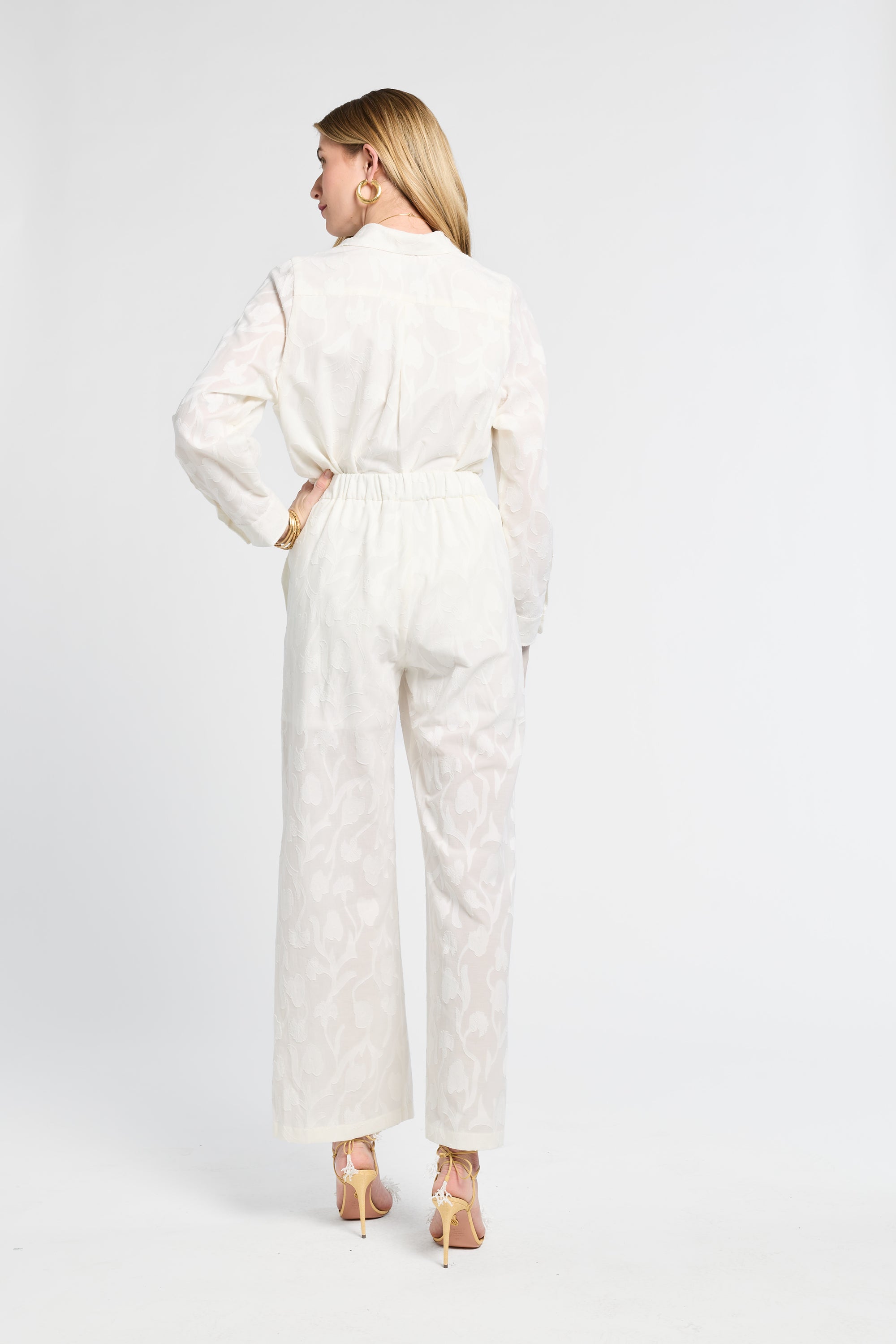 Woman modeling a long sleeve white floral blouse and full length white floral pants against a white backdrop