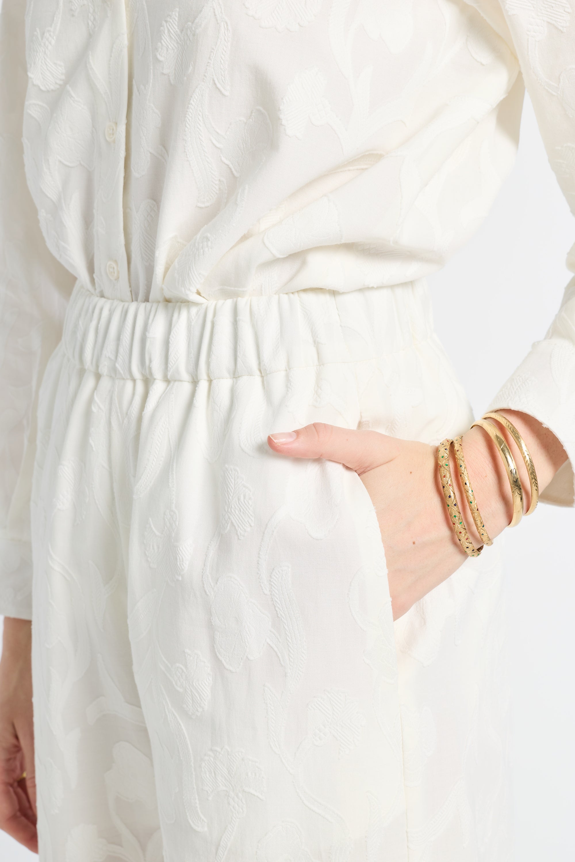 Image of a woman modeling white pants with floral detailing and gold jewelry