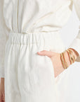 Image of a woman modeling white pants with floral detailing and gold jewelry
