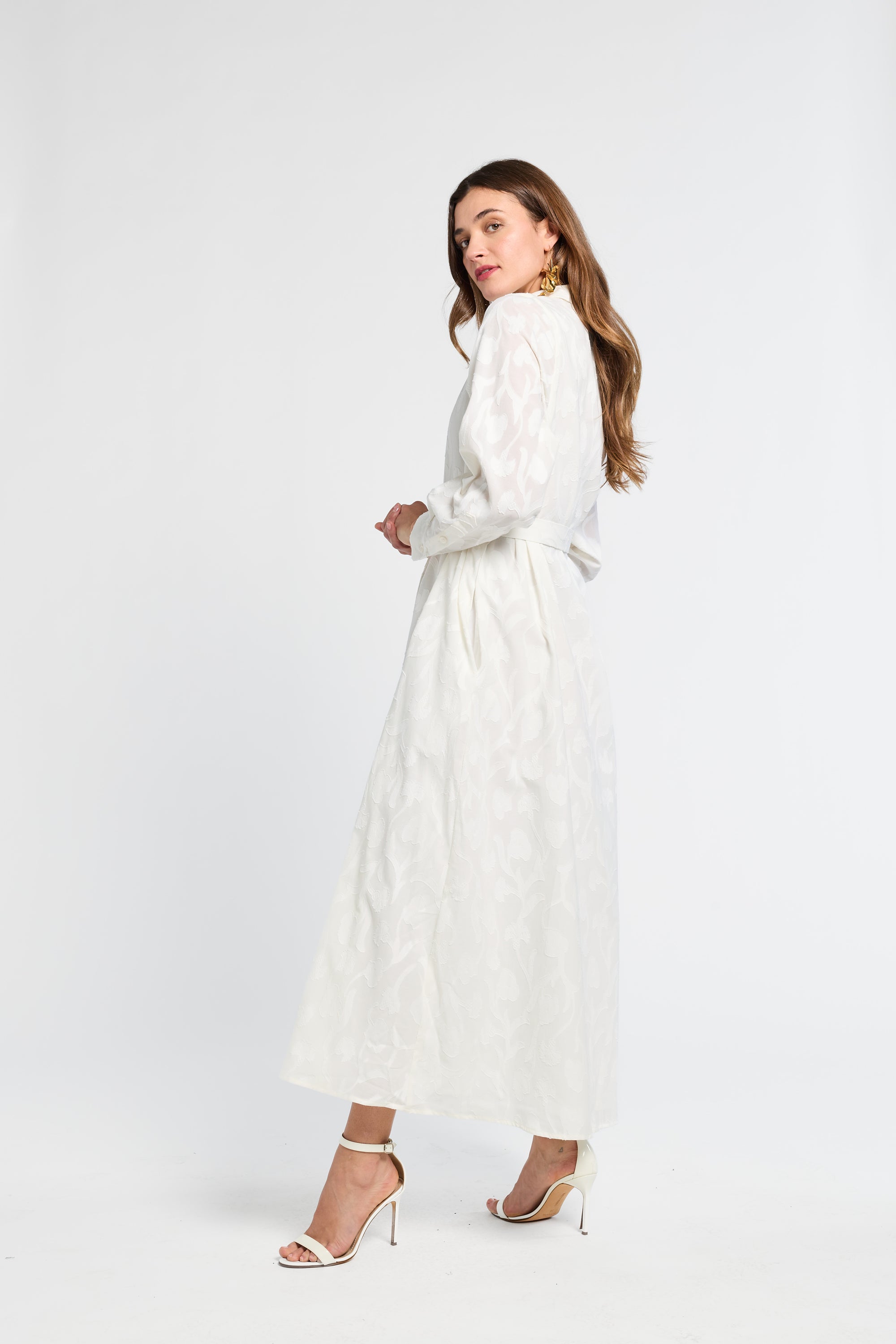 Woman wearing a white maxi dress with white heels on a white background
