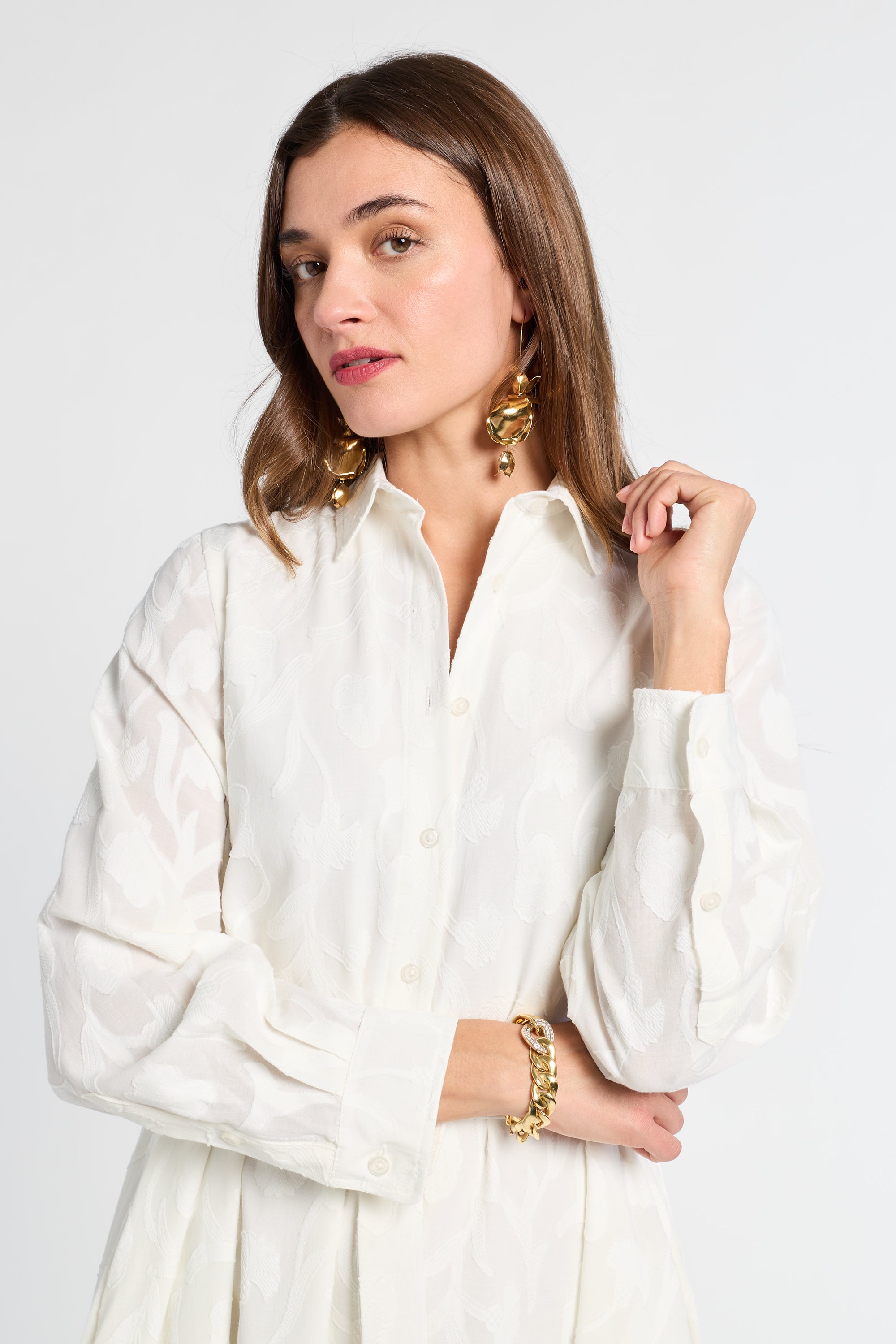 Woman wearing a white maxi dress with gold jewelry against a plain background