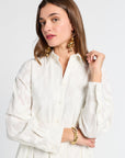 Woman wearing a white maxi dress with gold jewelry against a plain background