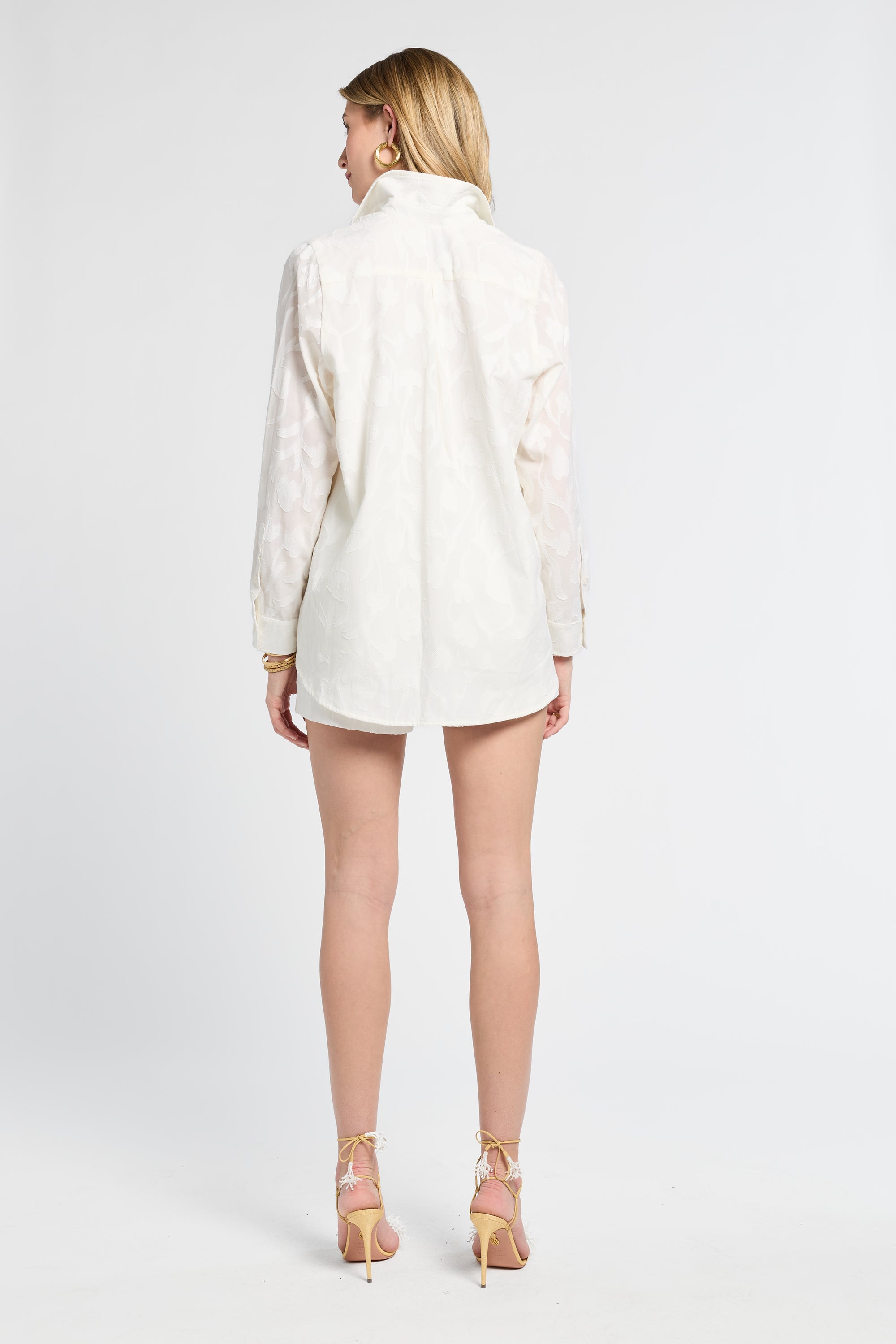 Woman modeling a long sleeve white floral blouse and the matching shorts on a white backdrop