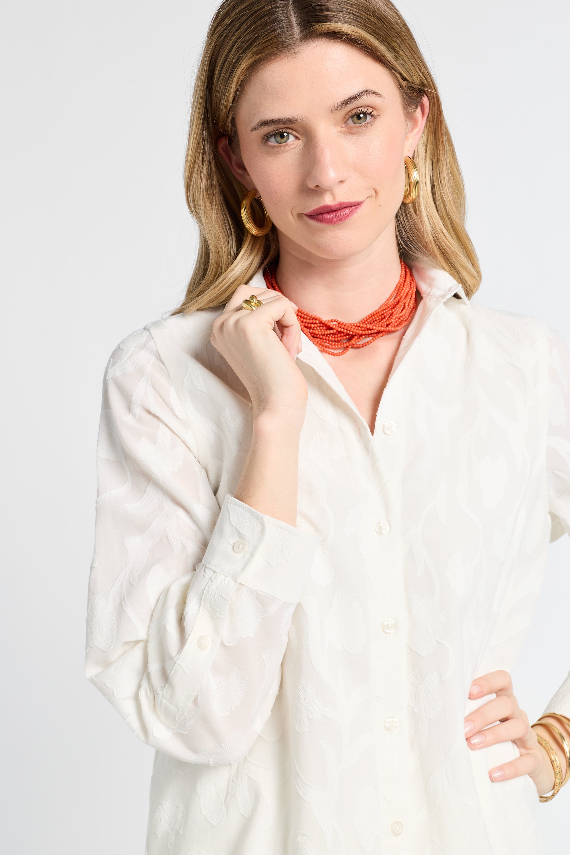 Woman wearing a white floral blouse and orange necklace against a plain background