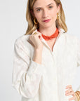 Woman wearing a white floral blouse and orange necklace against a plain background