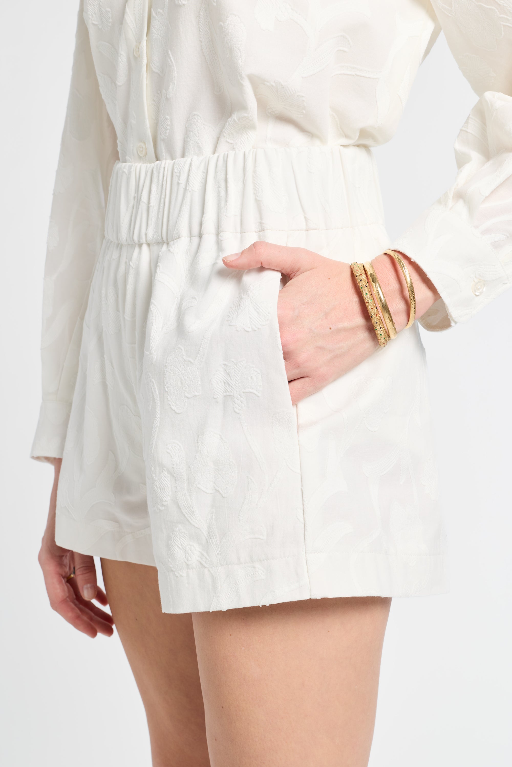 Close up image of a model wearing white floral shorts with gold jewelry on a white backdrop