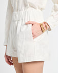 Close up image of a model wearing white floral shorts with gold jewelry on a white backdrop