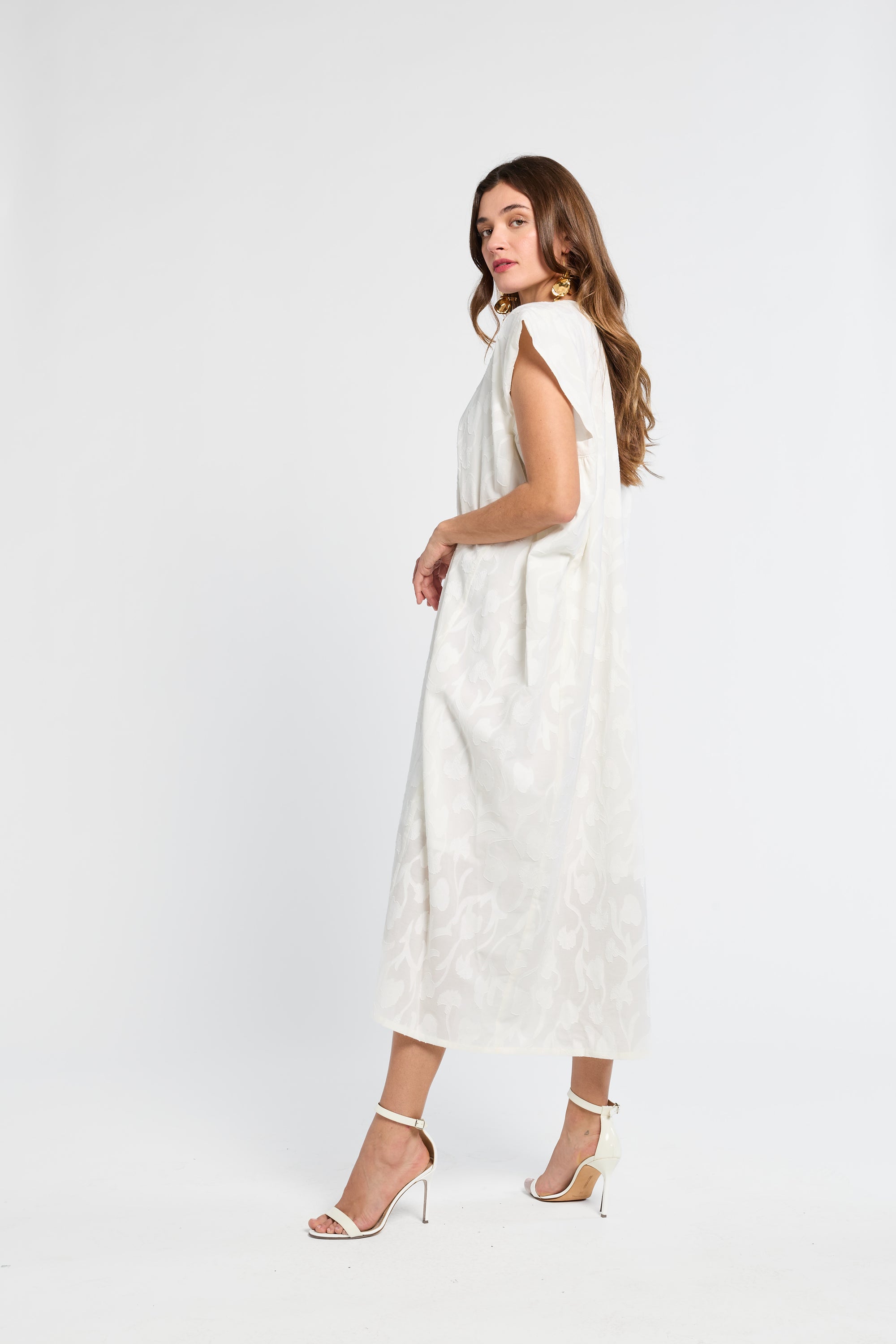 Woman wearing a white caftan and white heels on a white background