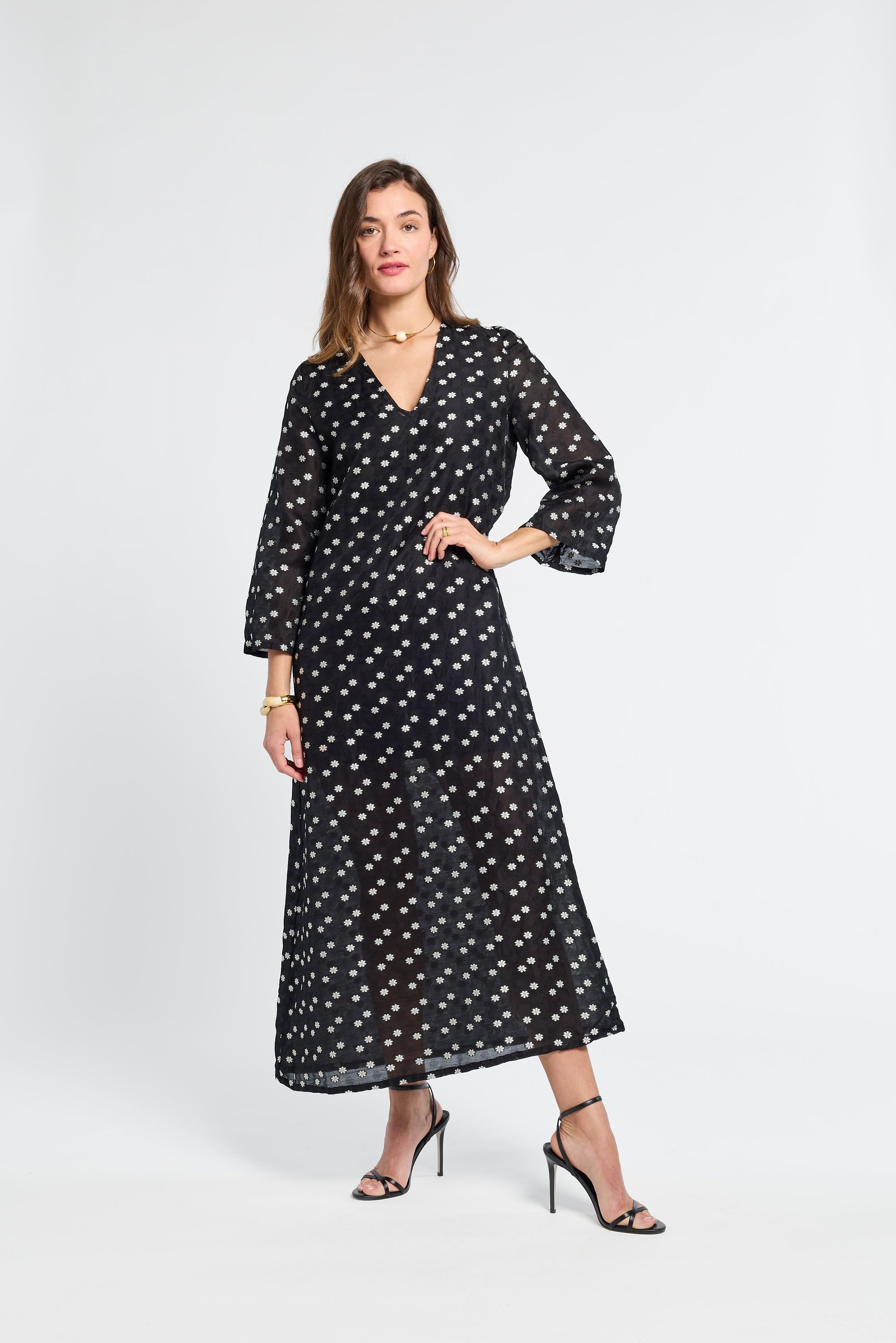 Woman wearing a sheer black caftan with white flowers on a white background
