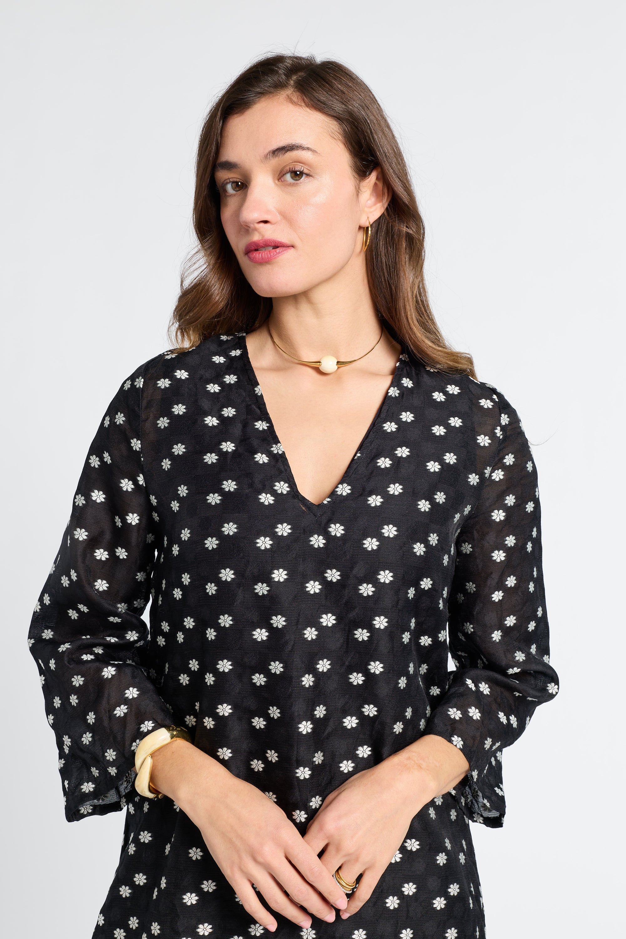 Woman wearing a sheer black dress with white floral pattern on a light gray background