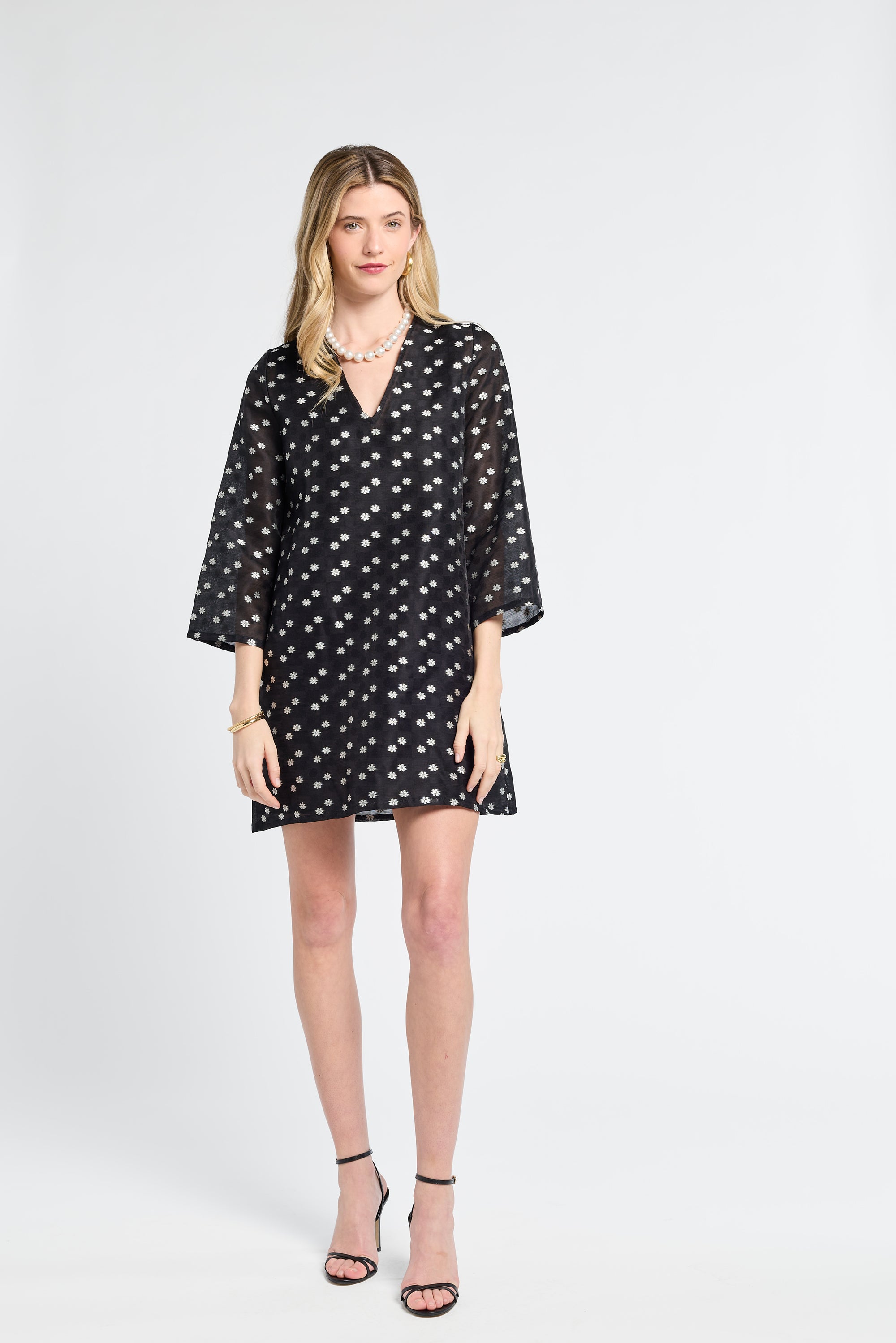 Woman wearing a black caftan dress with white flower detailing on a white background