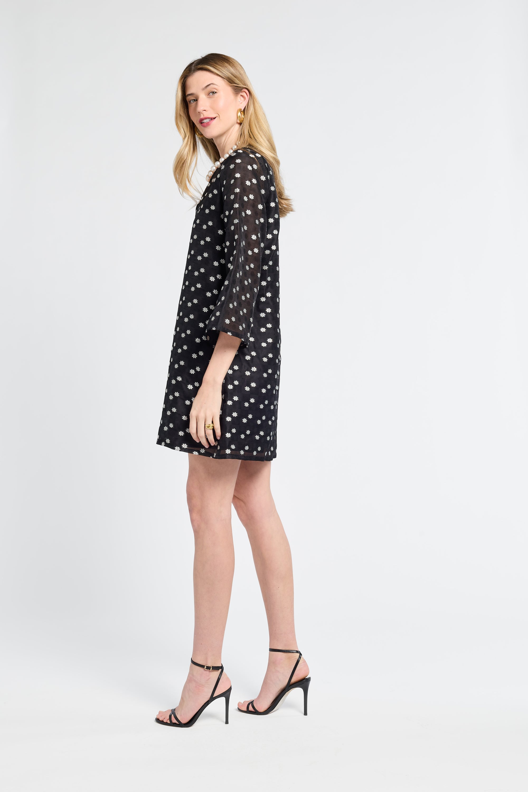 Woman wearing a sheer black dress with little white flowers on a white background
