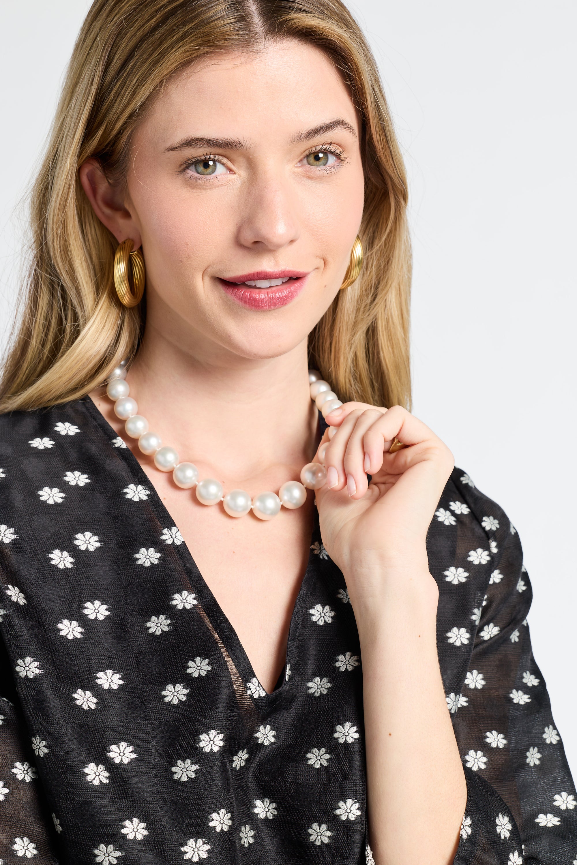 Woman wearing a pearl necklace with a sheer black dress with floral detailing on a white background