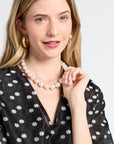 Woman wearing a pearl necklace with a sheer black dress with floral detailing on a white background