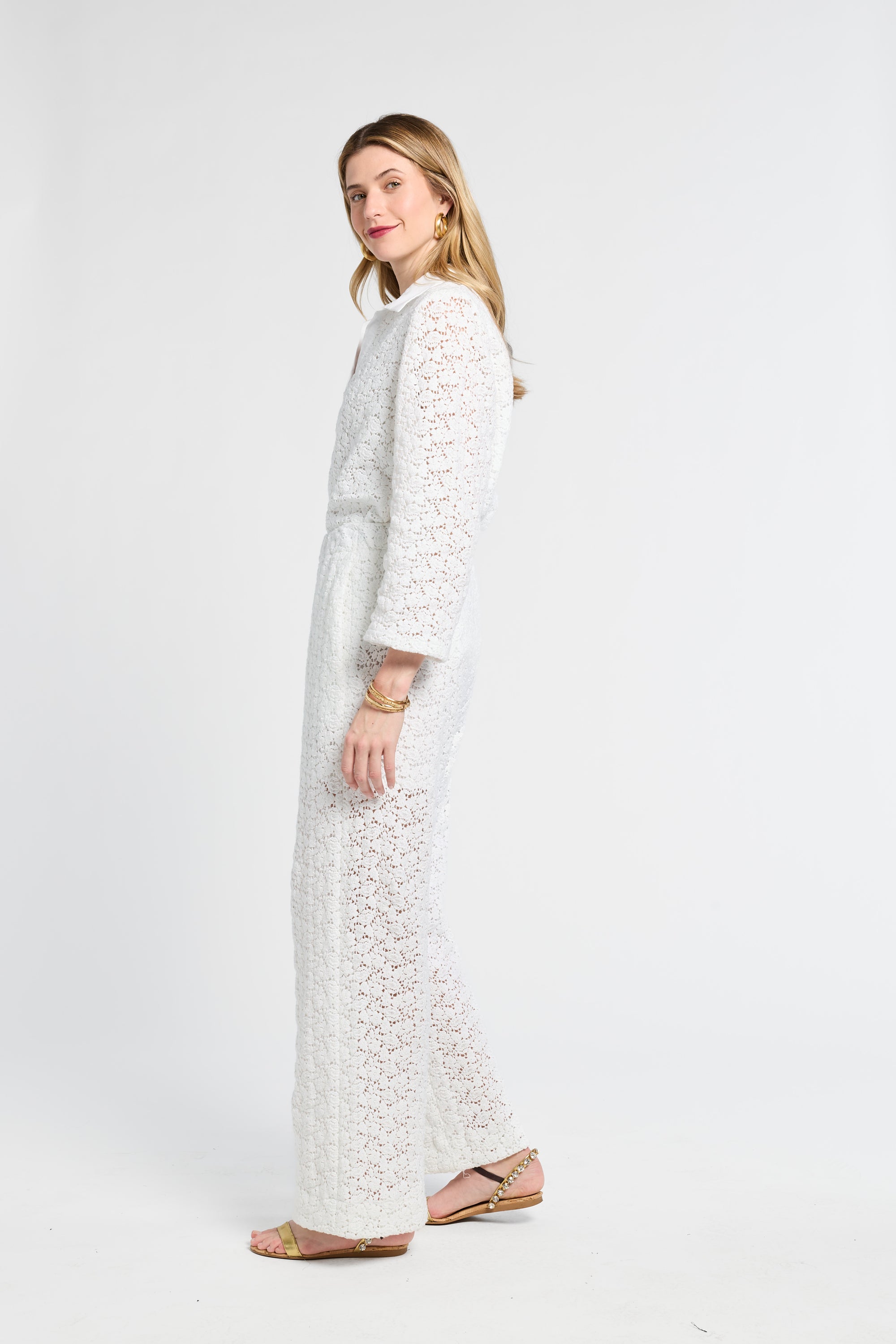 Woman modeling white pants with lace details on a white background