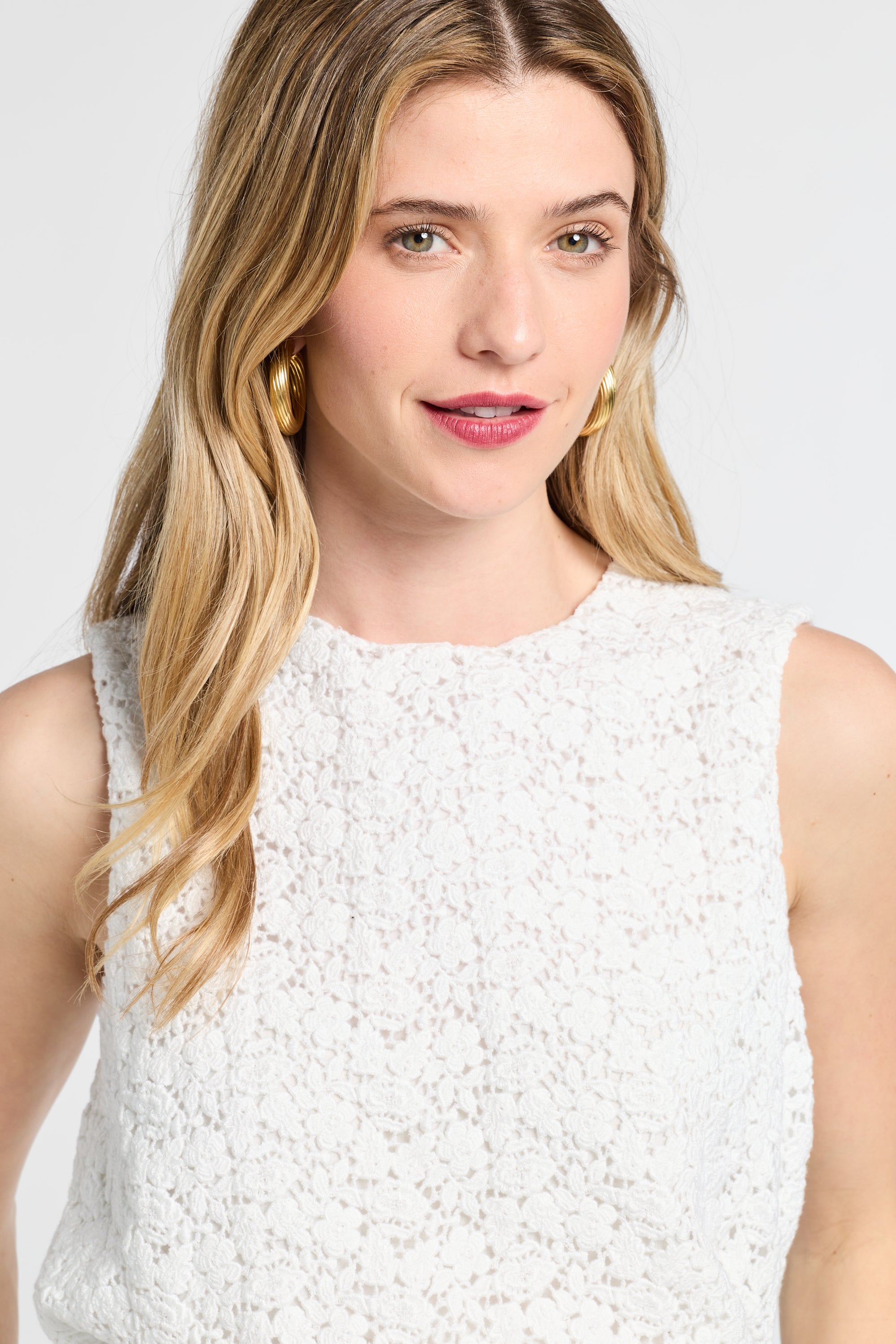 Woman wearing a lace white sleeveless blouse with a plain background