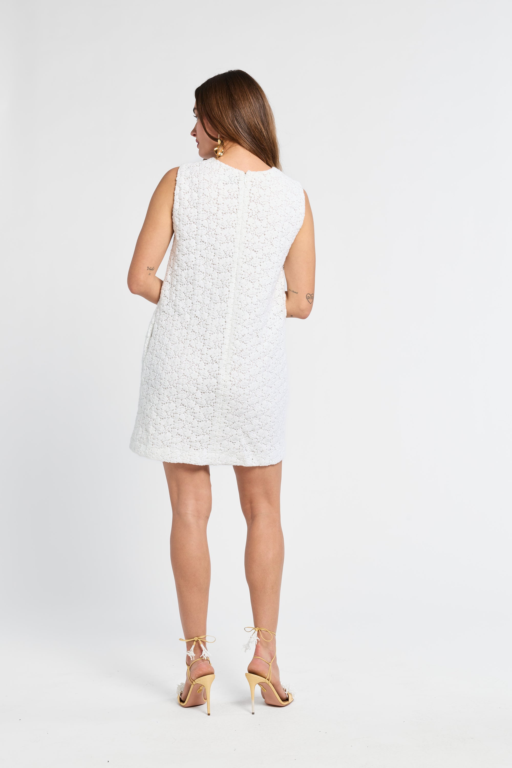 Woman modeling a white sleeveless mini dress on a plain background