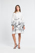 Woman modeling a long sleeve white dress with black floral detailing along the bottom on a white backdrop