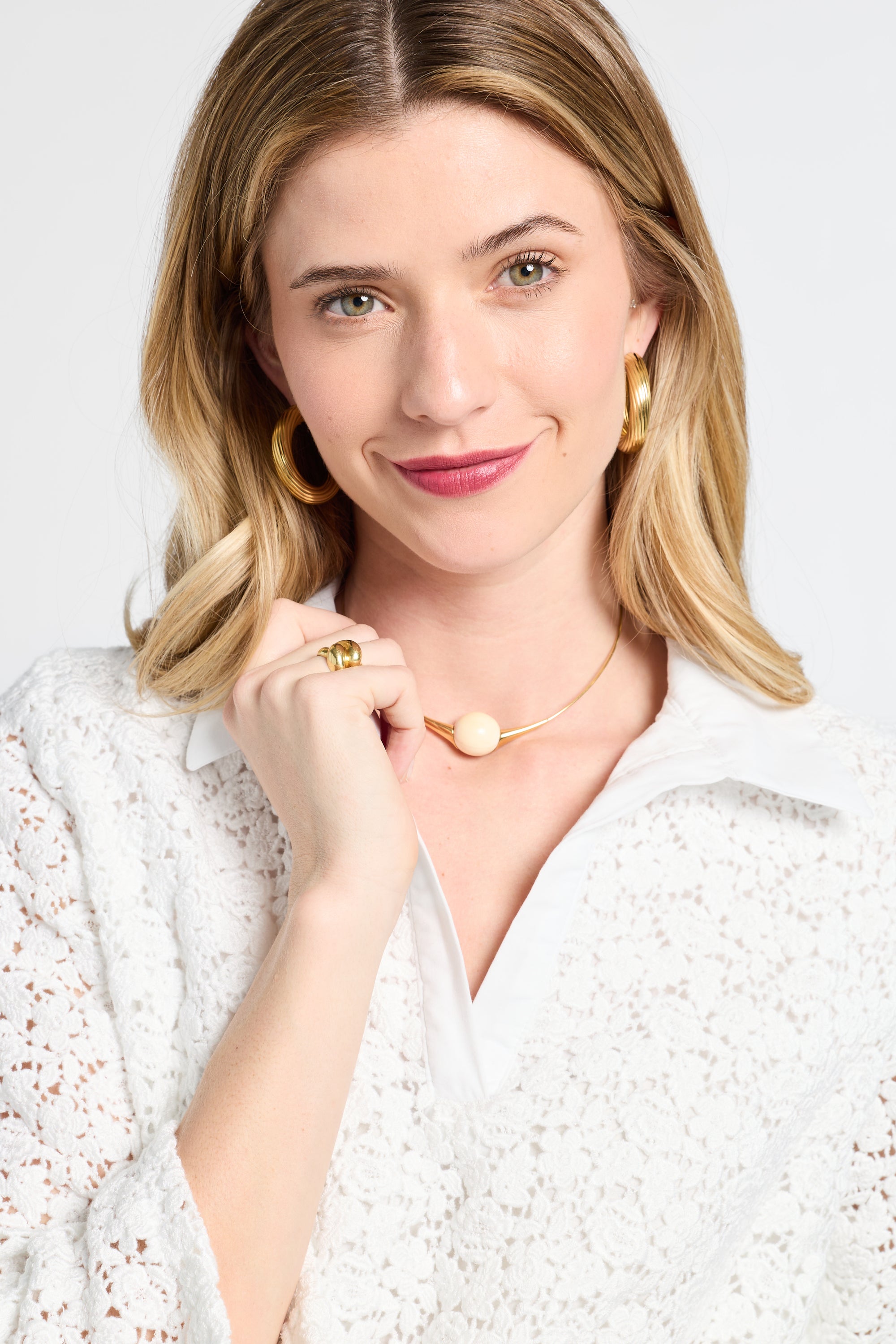 Woman wearing gold jewelry and a white lace blouse against a white background