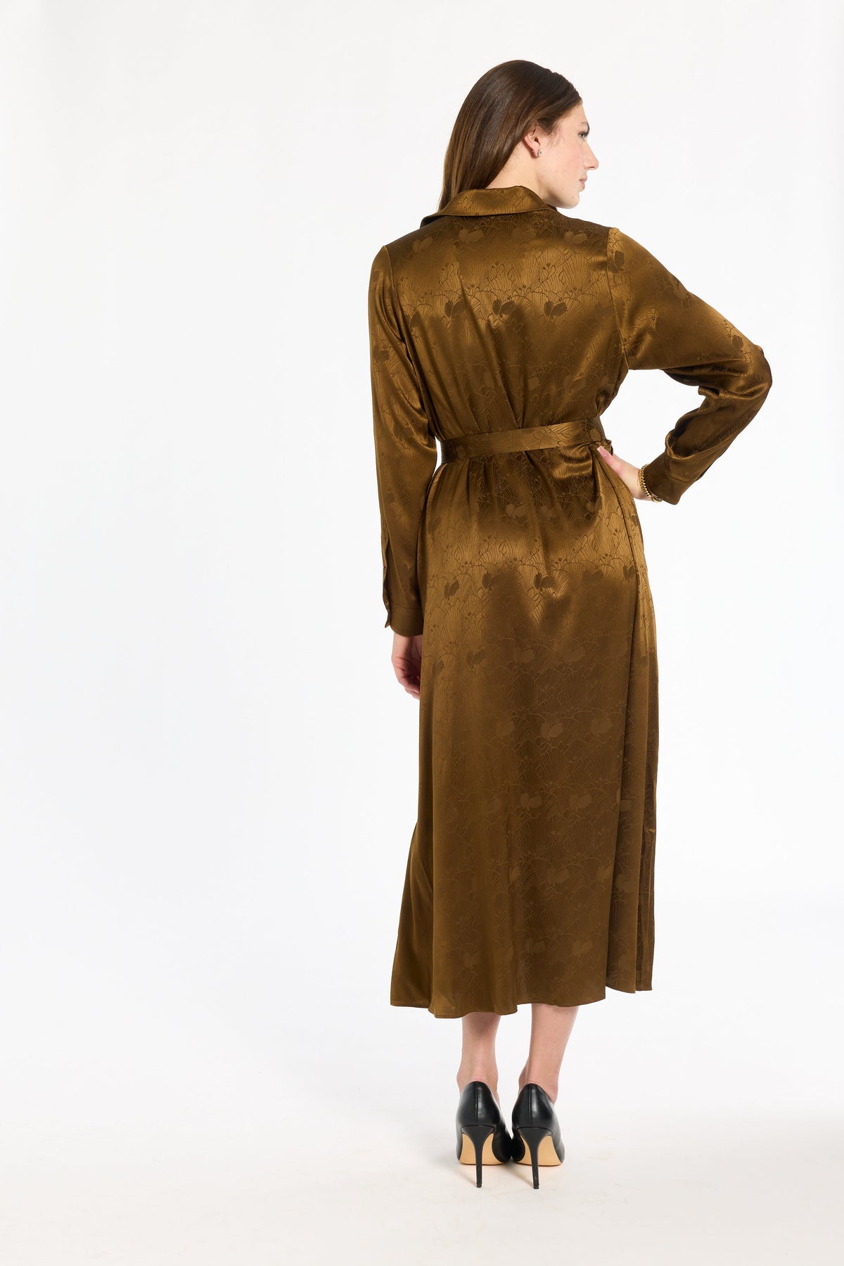 A woman modeling the Golden Umber Eleanor Shirt Dress with a tied sash and black heels, back view, photographed against a plain white studio background.
