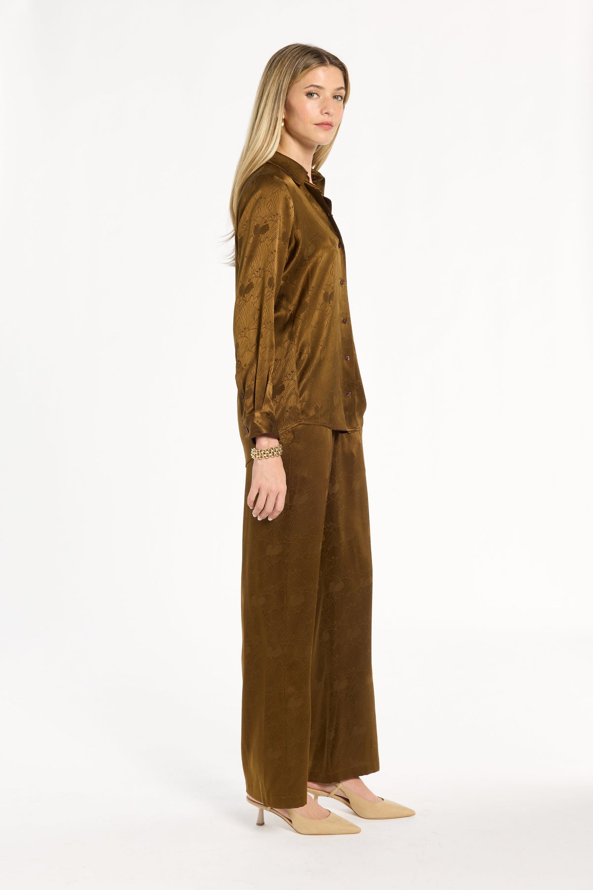A woman modeling the Golden Umber Eleanor Shirt with coordinating Diane Pants, three-quarter side view, photographed against a plain white studio background.