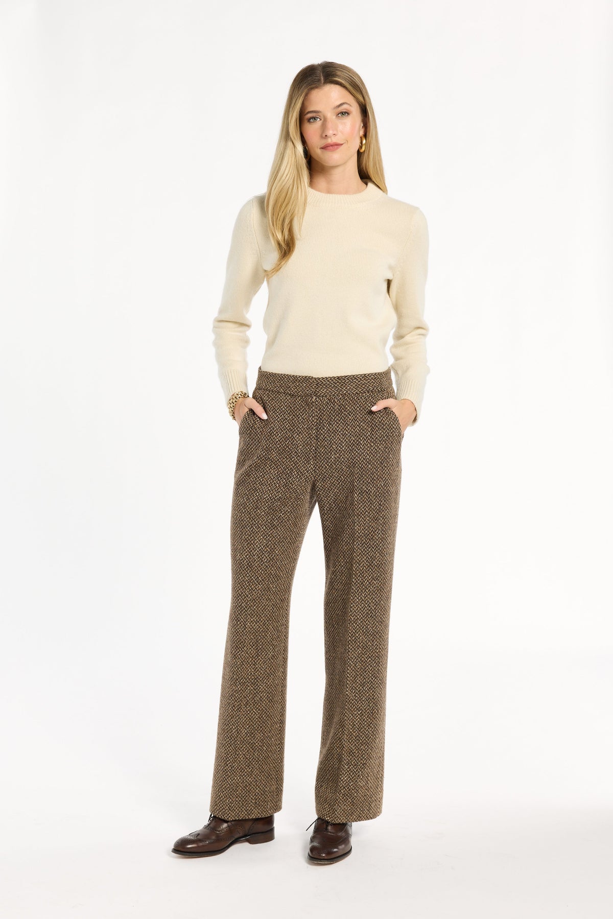 A woman modeling the Tobacco Tweed Ellis Pants with a cream sweater and brown loafers, front view with hands in pockets, photographed against a plain white studio background.