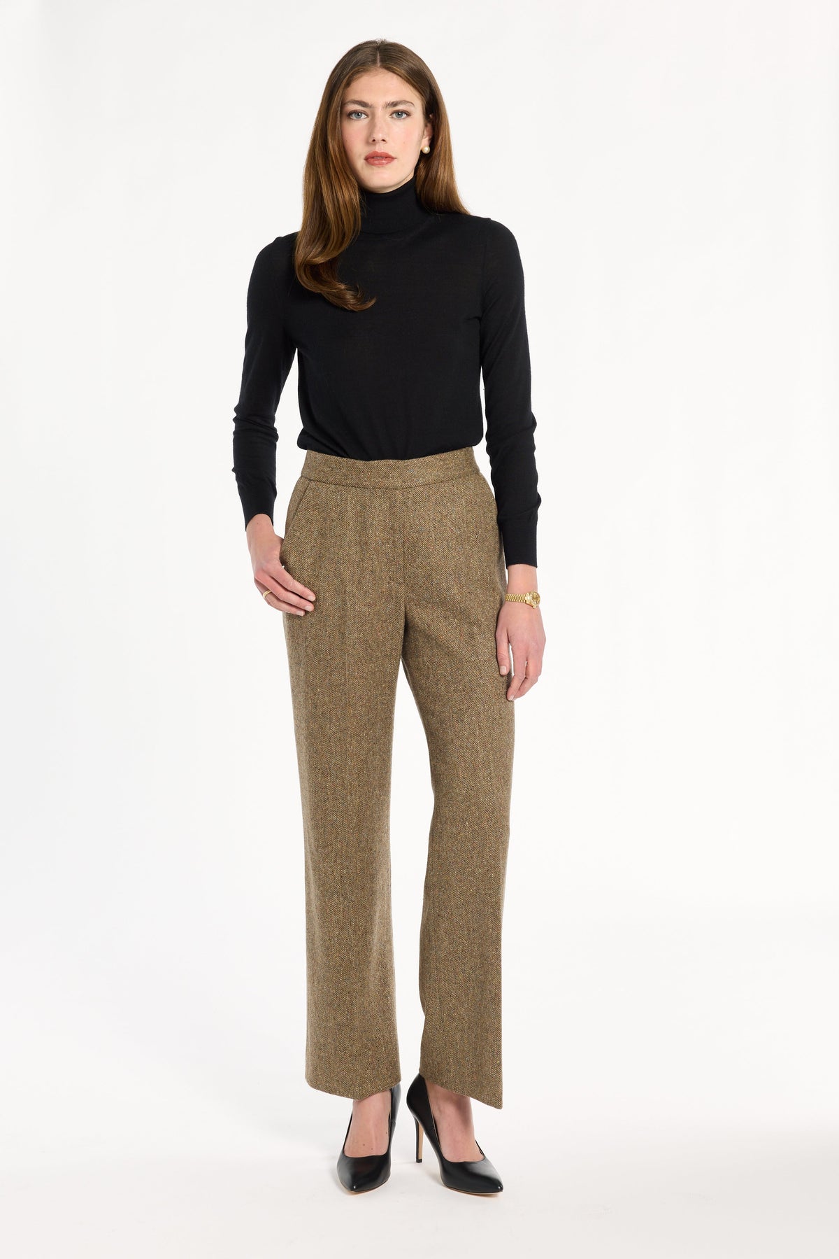 A woman modeling the Painter's Fleck Herringbone Ellis Pants with a black turtleneck and black heels, front view, photographed against a plain white studio background.