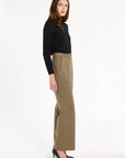 A woman modeling the Painter's Fleck Herringbone Ellis Pants with a black turtleneck and heels, side view, photographed against a plain white studio background.