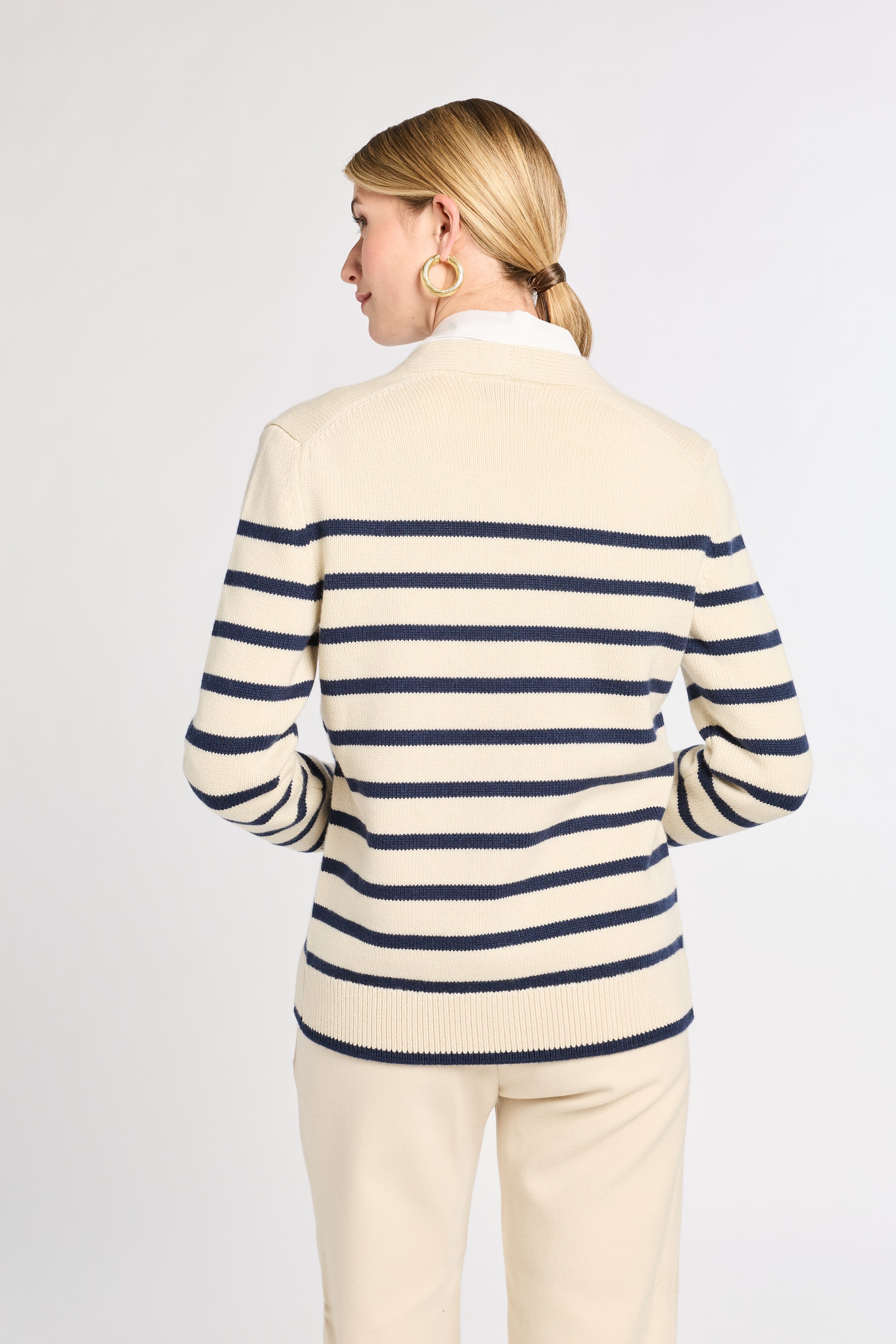 Woman wearing a cream and navy striped sweater with a plain background