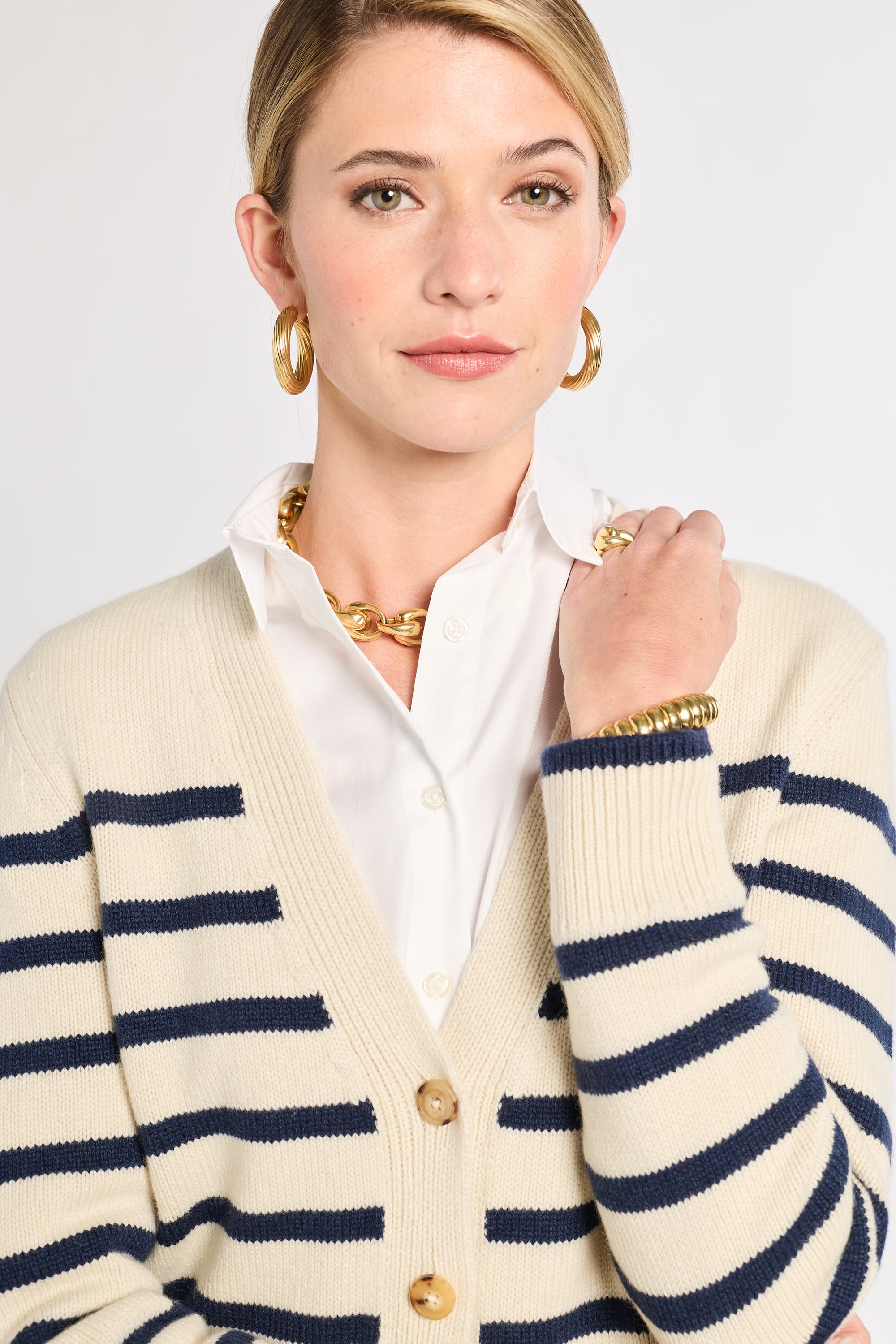 Woman wearing a cream cardigan with blue stripes over a white shirt on a plain background