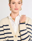 Woman wearing a cream cardigan with blue stripes over a white shirt on a plain background