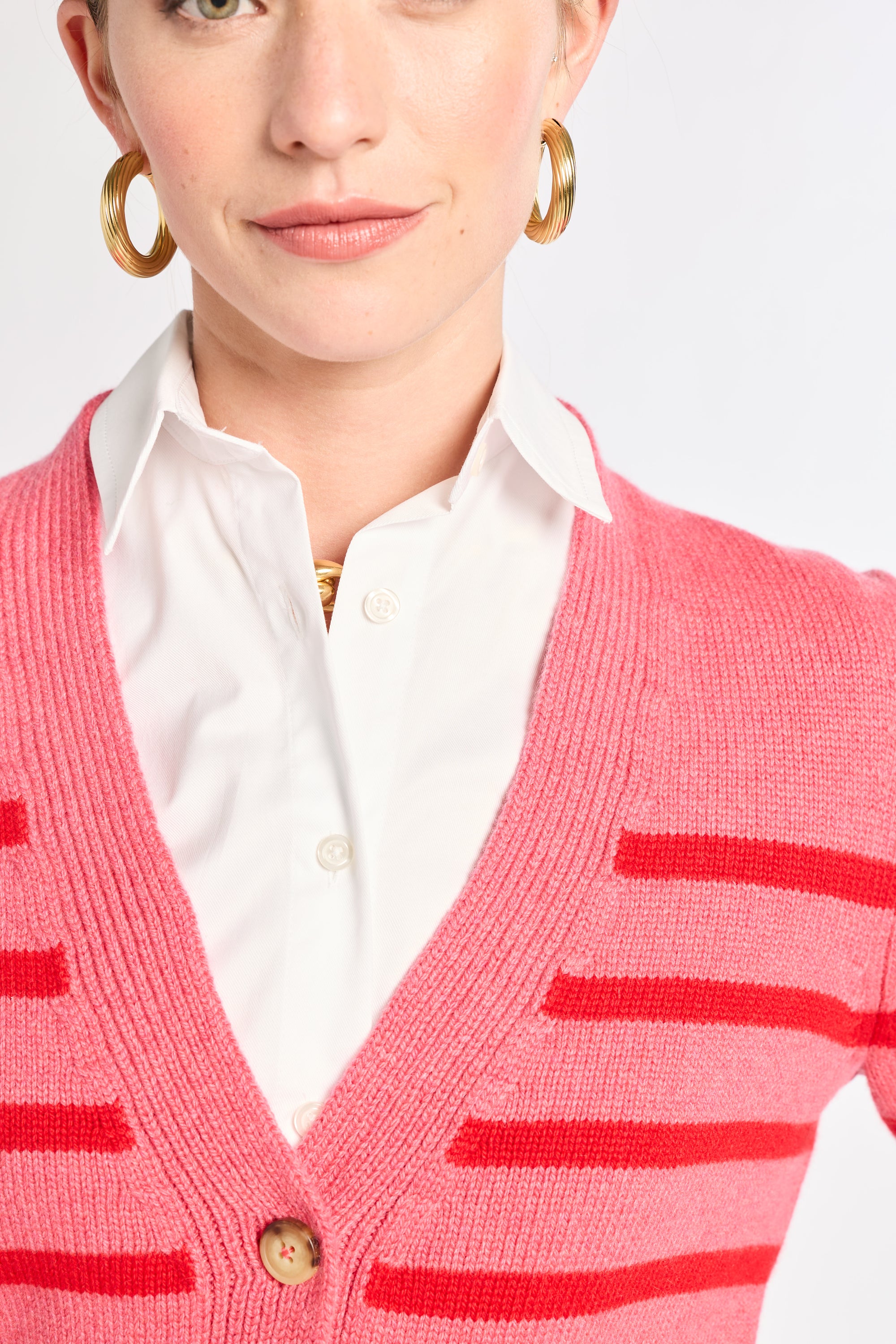 Person wearing a pink cardigan with red stripes over a white shirt.