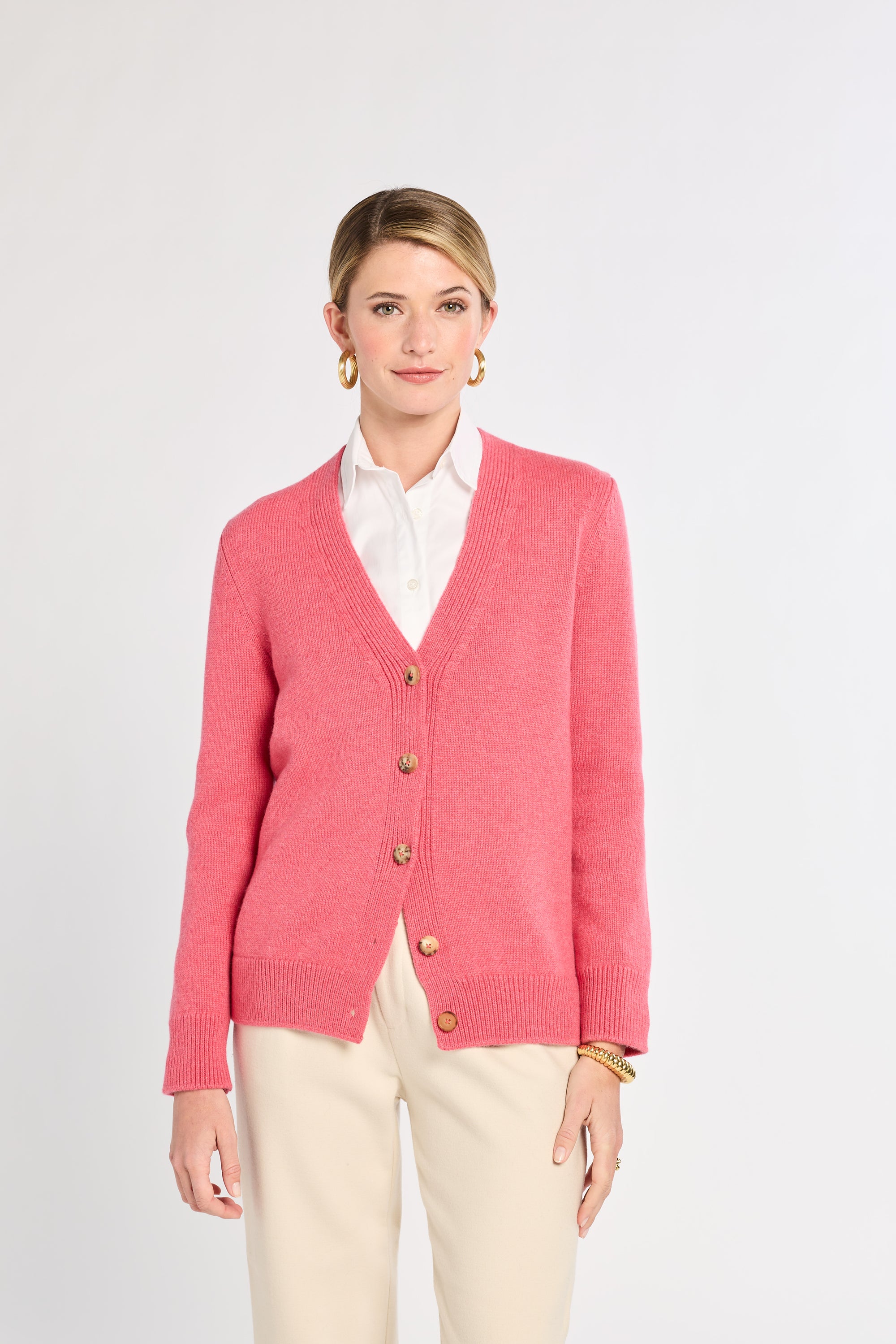 Woman wearing a pink cardigan with gold buttons on a white background