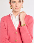 Woman wearing a pink cardigan over a white shirt on a plain background
