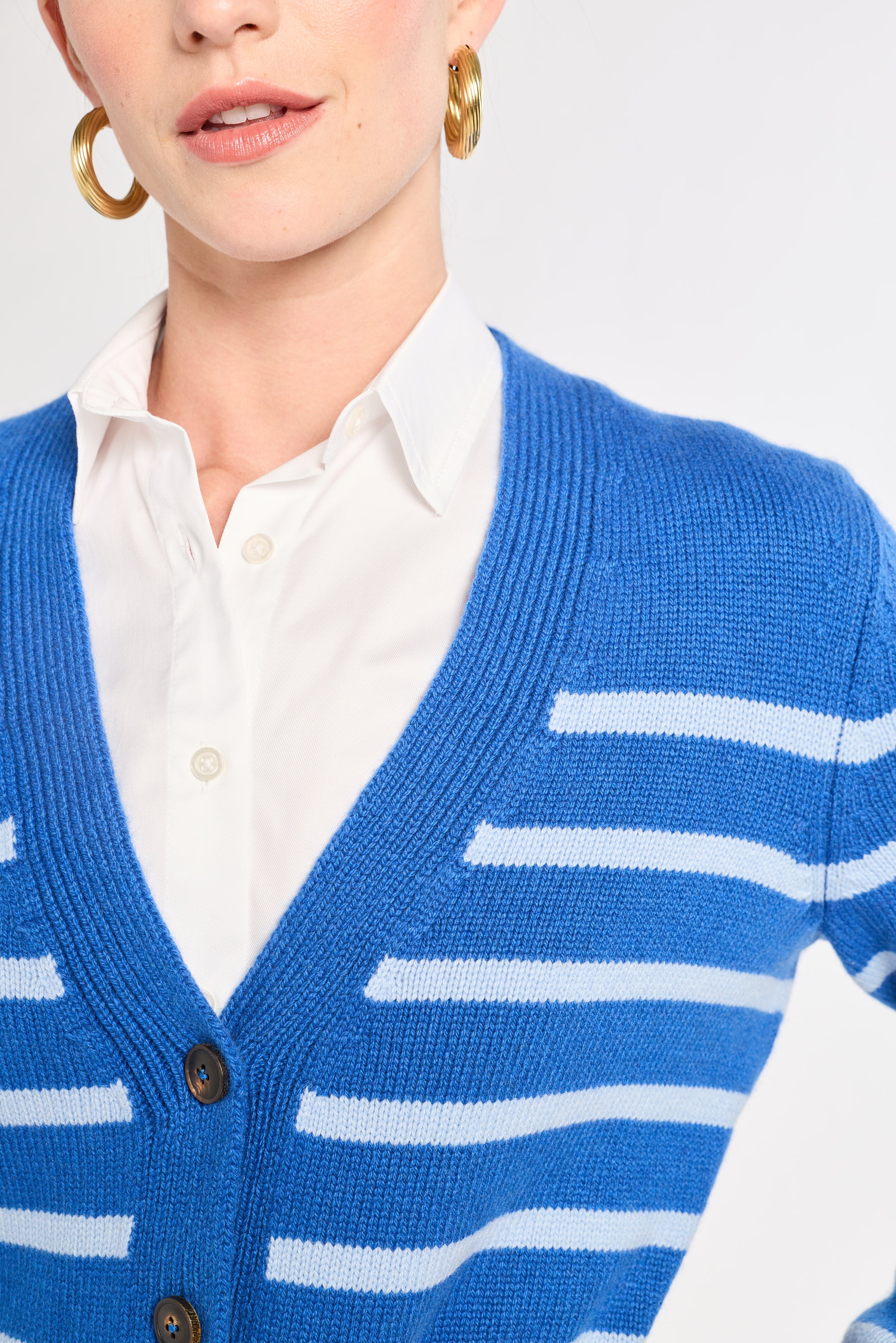 Person wearing a blue cardigan with white stripes over a white shirt on a light gray background
