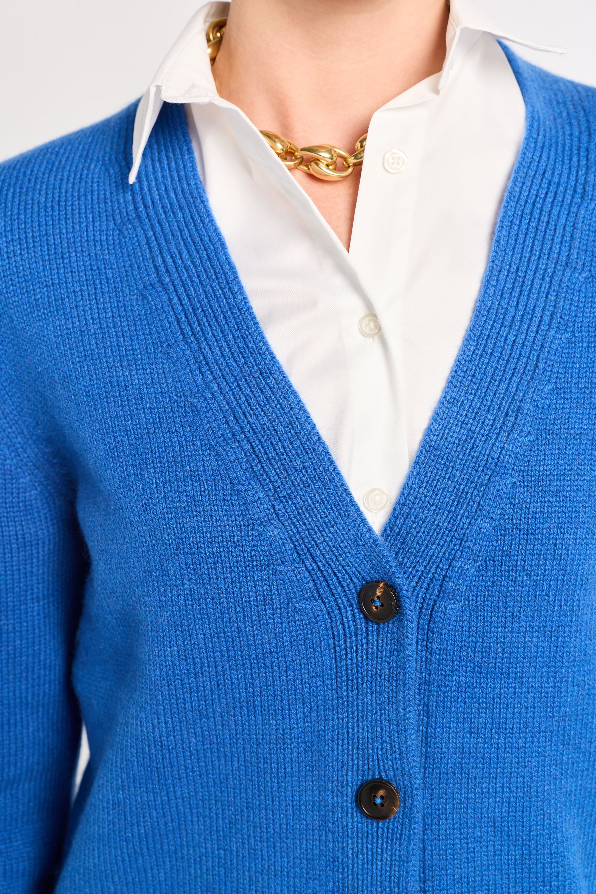 Blue cardigan over a white shirt with a gold necklace on a neutral background