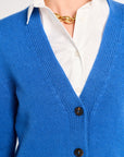 Blue cardigan over a white shirt with a gold necklace on a neutral background