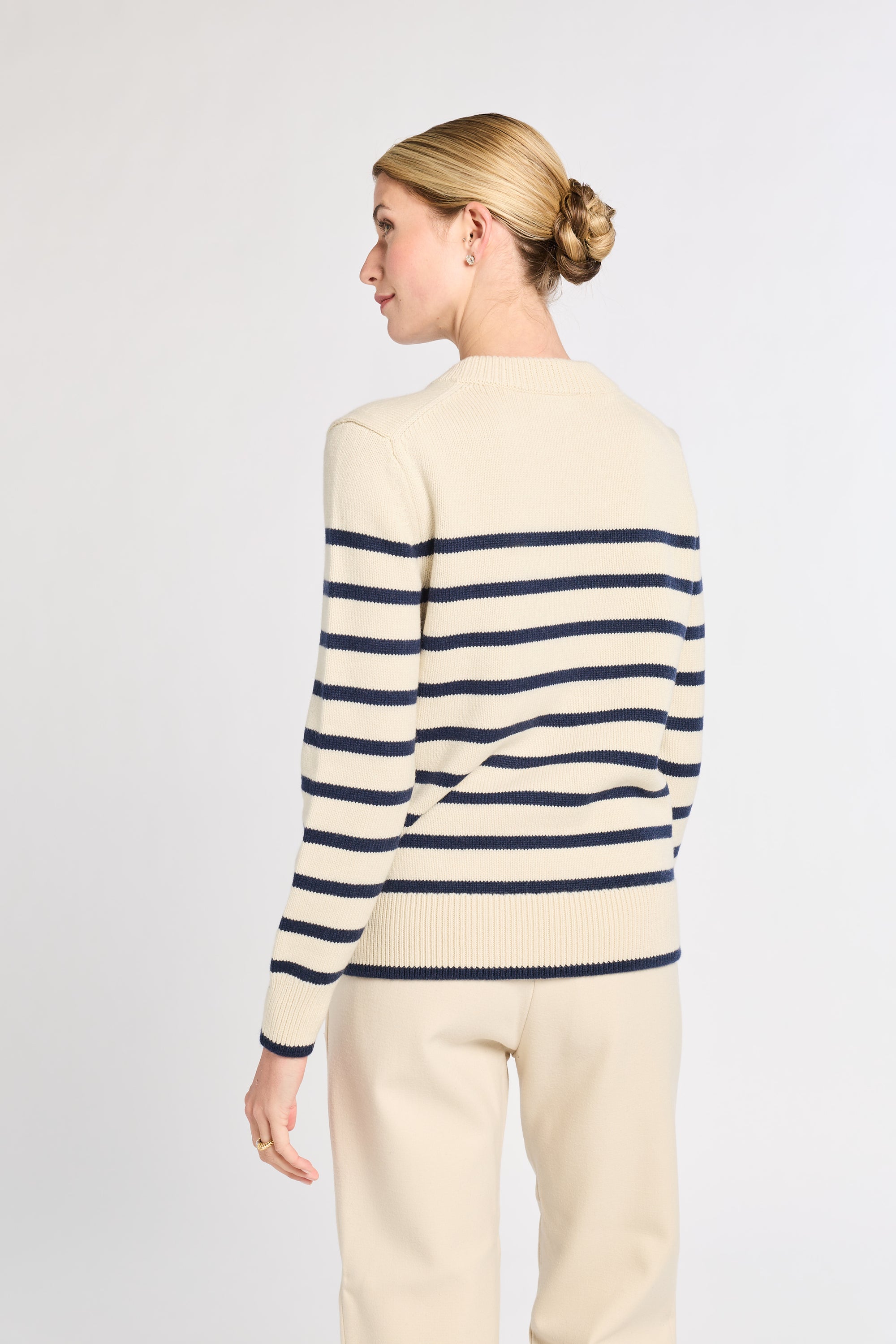 Woman wearing a cream and navy striped sweater on a plain background