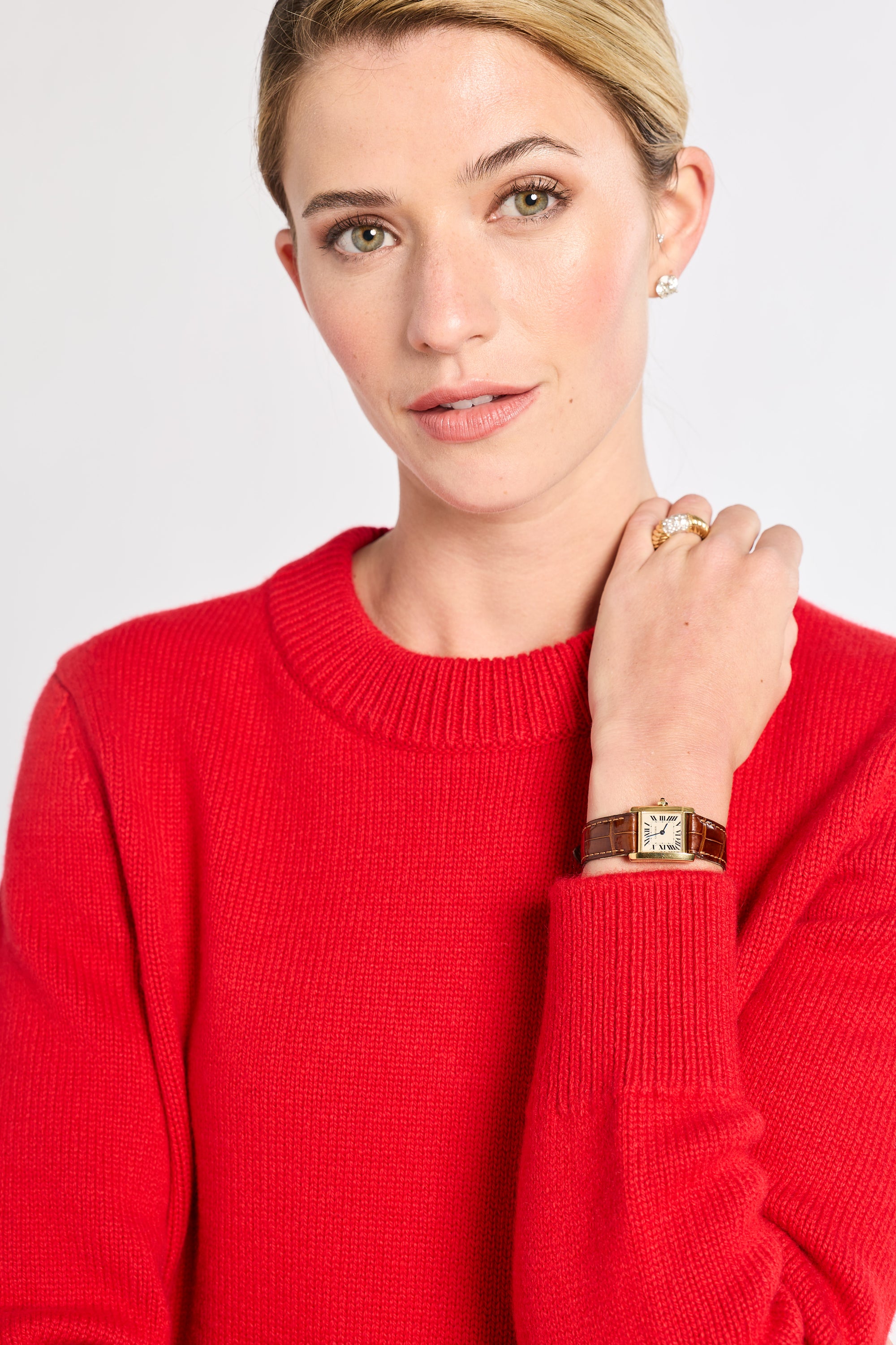 Woman wearing a red sweater with a gold watch and ring on a white background