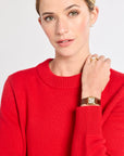 Woman wearing a red sweater with a gold watch and ring on a white background