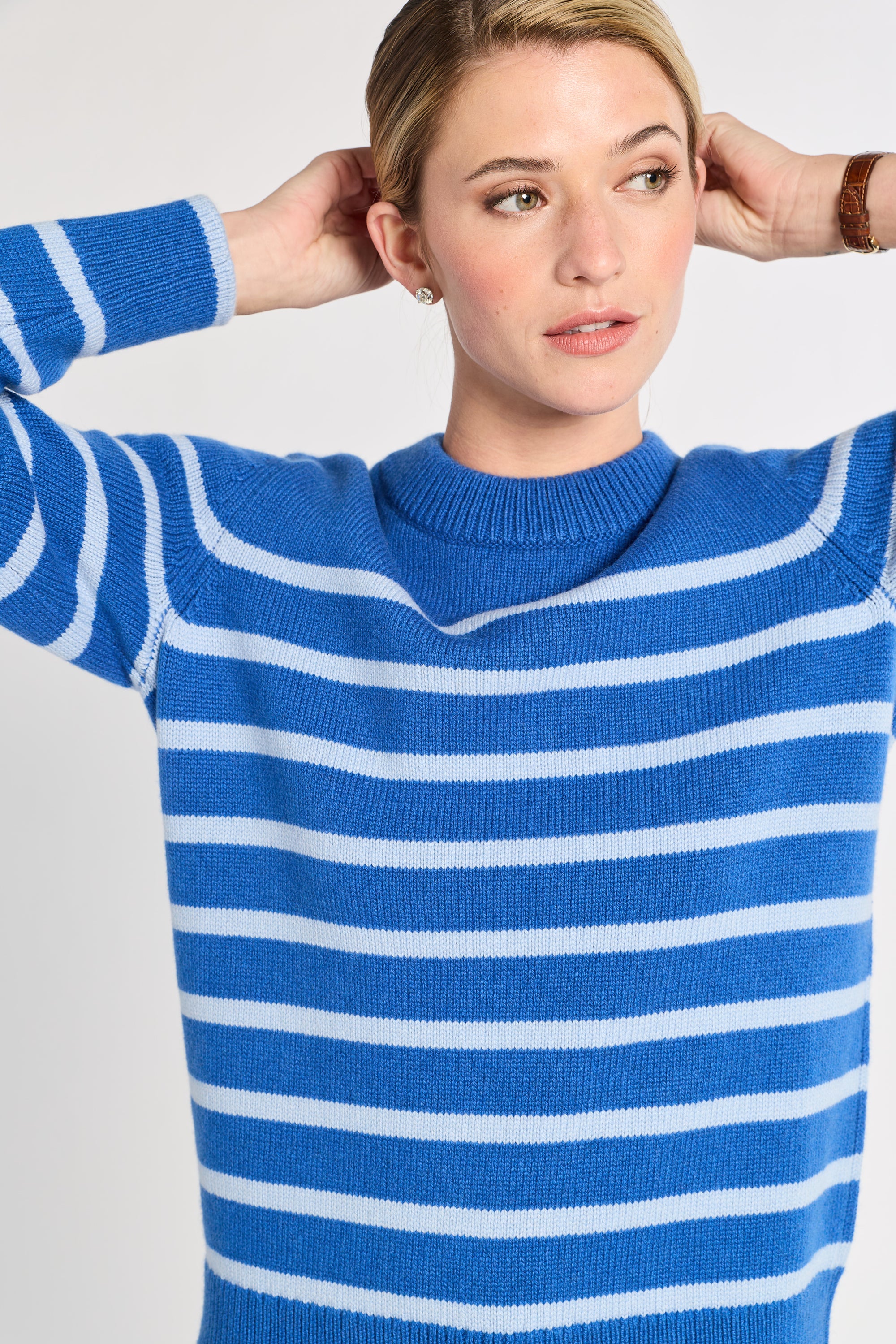 Woman wearing a blue and light blue striped sweater against a light background