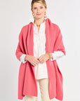 Woman wearing a pink shawl over a white shirt and beige pants on a light gray background
