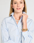 Woman wearing a light blue striped shirt with jewelry on a plain background