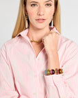 Woman wearing a pink shirt with colorful beaded bracelet on a plain background
