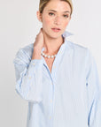 Woman wearing a light blue striped shirt with a pearl necklace on a plain background