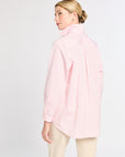 Woman wearing a light pink button-up shirt and beige pants on a white background